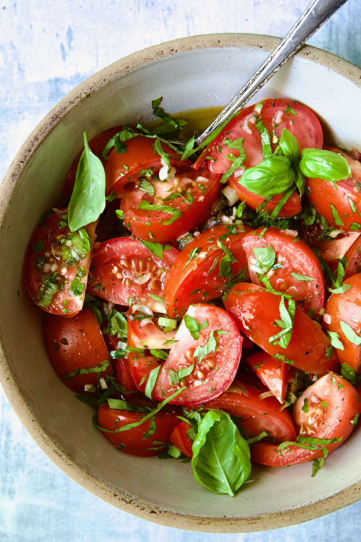 Marinated Tomatoes in old clay bowl with serving spoon garnished with fresh parsley.
