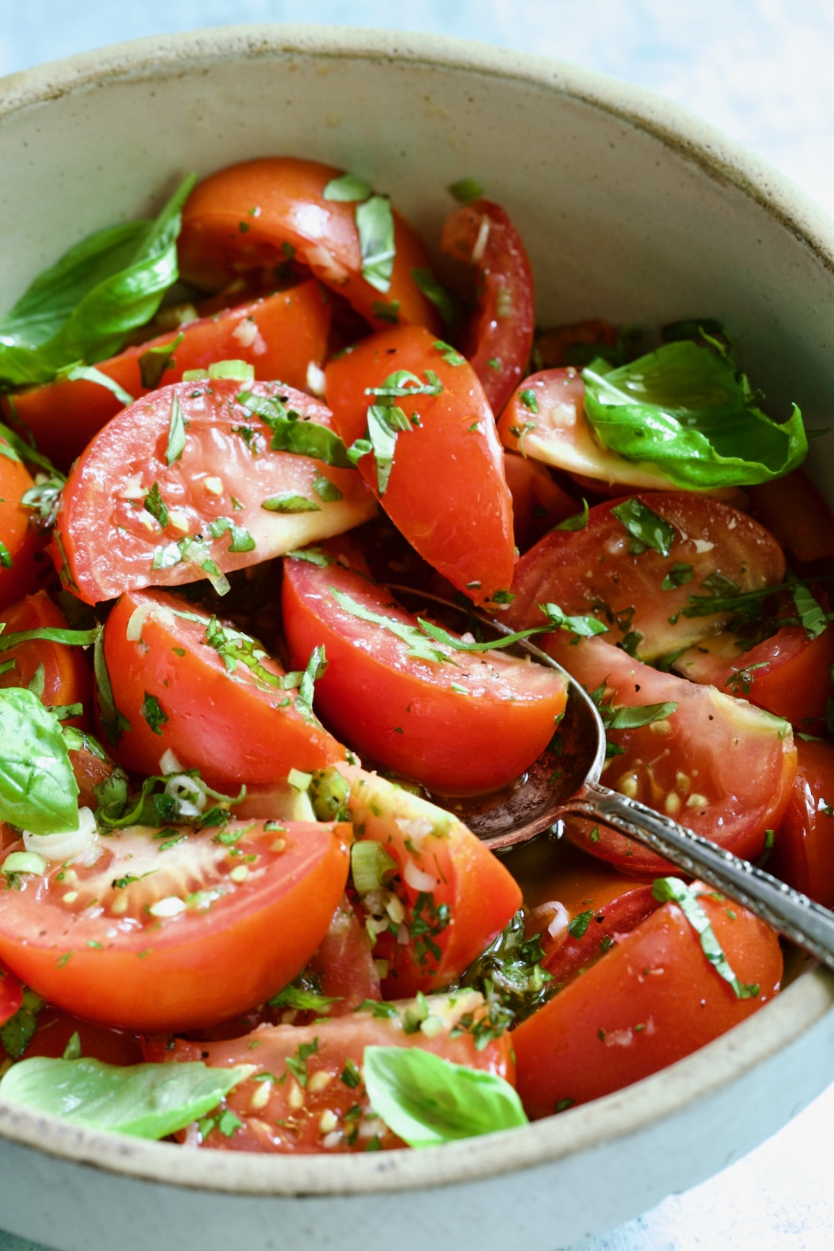 Marinated Tomatoes in old clay bowl with serving spoon garnished with fresh parsley.