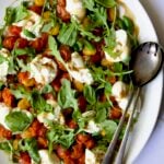 Roasted Cherry Tomato Burrata Caprese Salad on white oval platter with serving utensils.