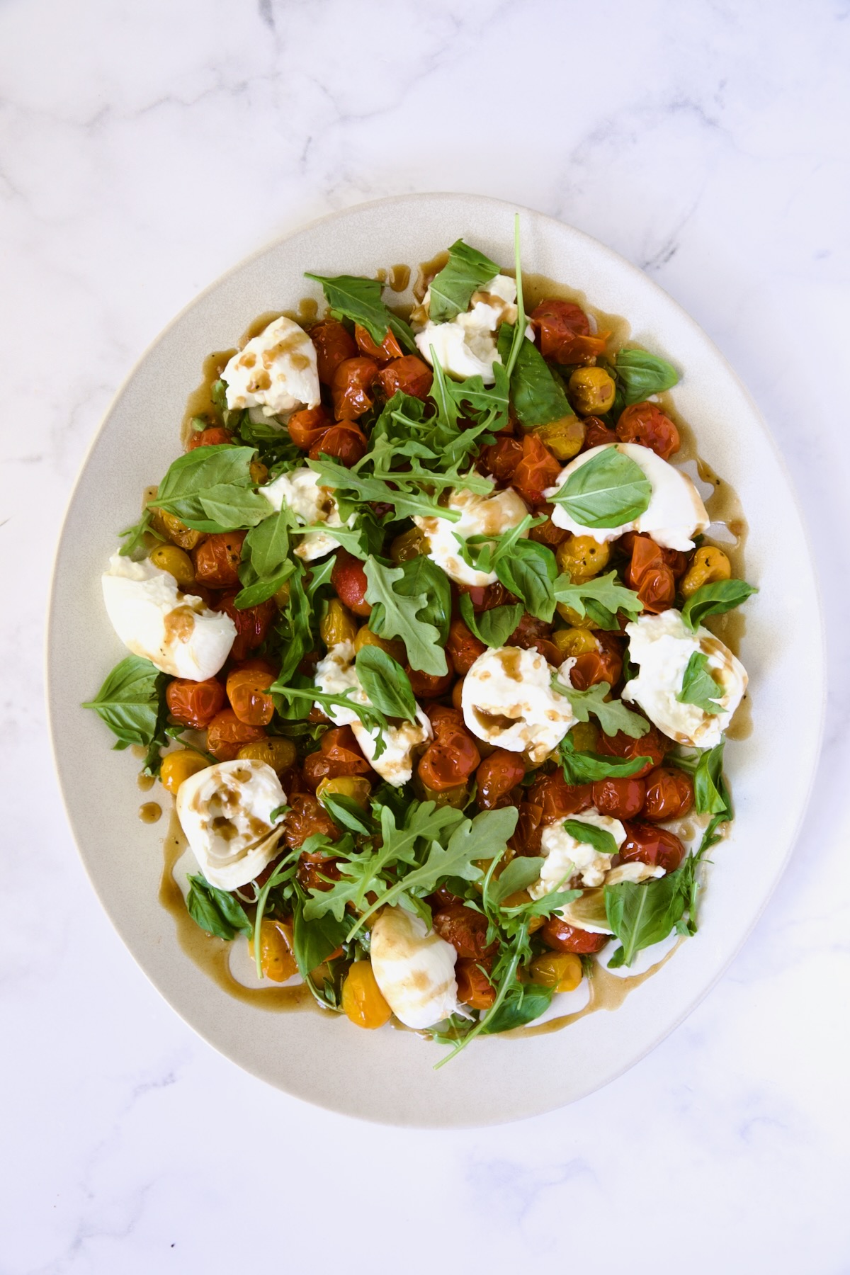 Roasted Cherry Tomato Burrata Caprese Salad on white oval platter.