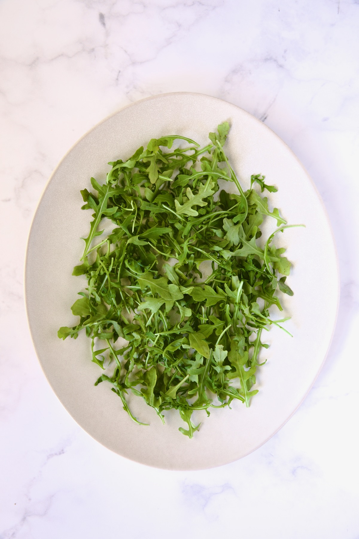 Fresh arugula on white oval platter.