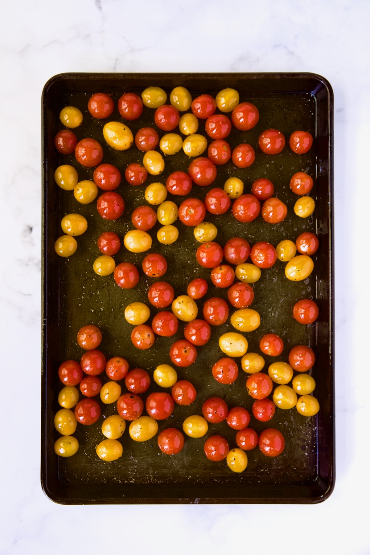 Red and yellow cherry tomatoes on rimmed baking sheet before being roasted.