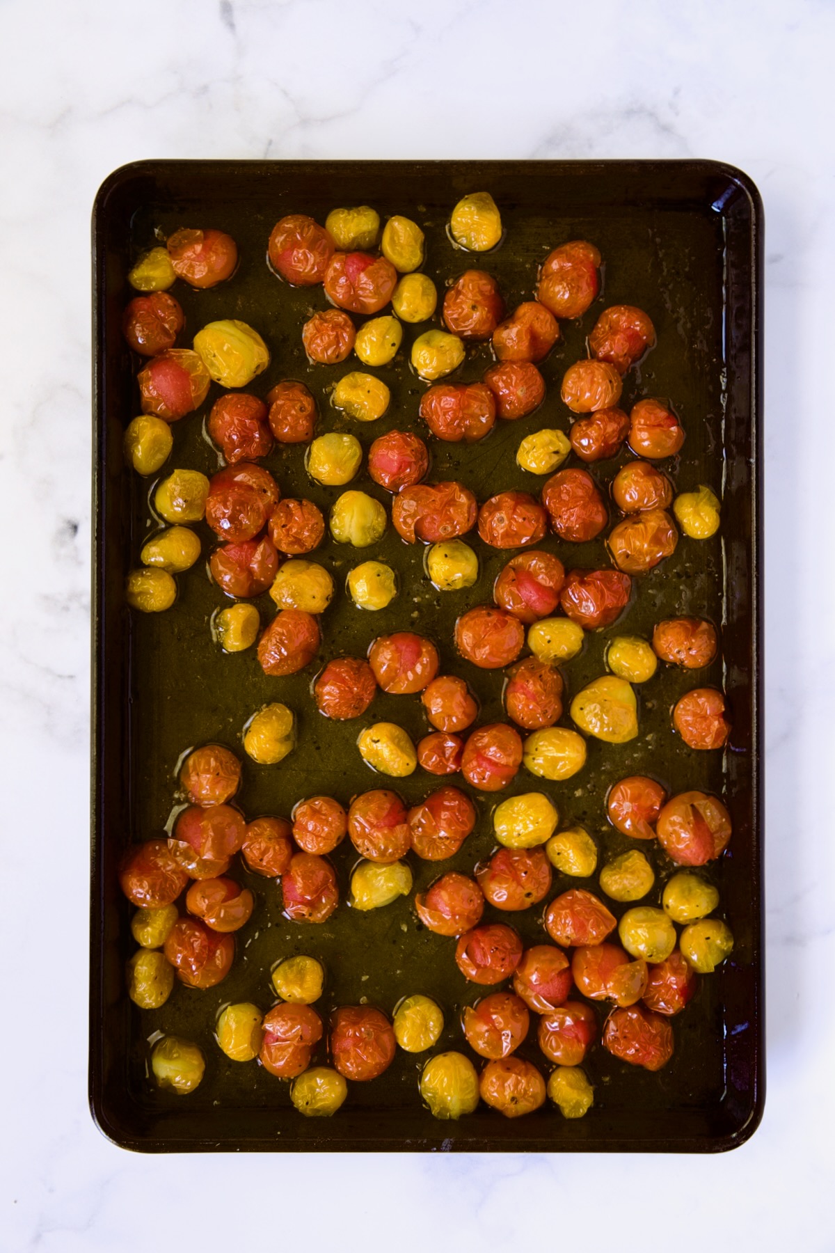 Red and yellow cherry tomatoes on rimmed baking sheet after being roasted.