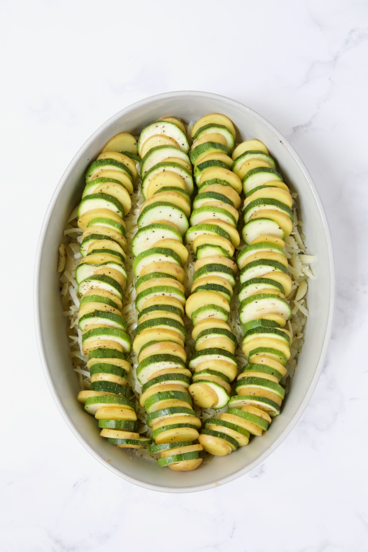 Sliced potatoes and zucchini in oval baking dish.