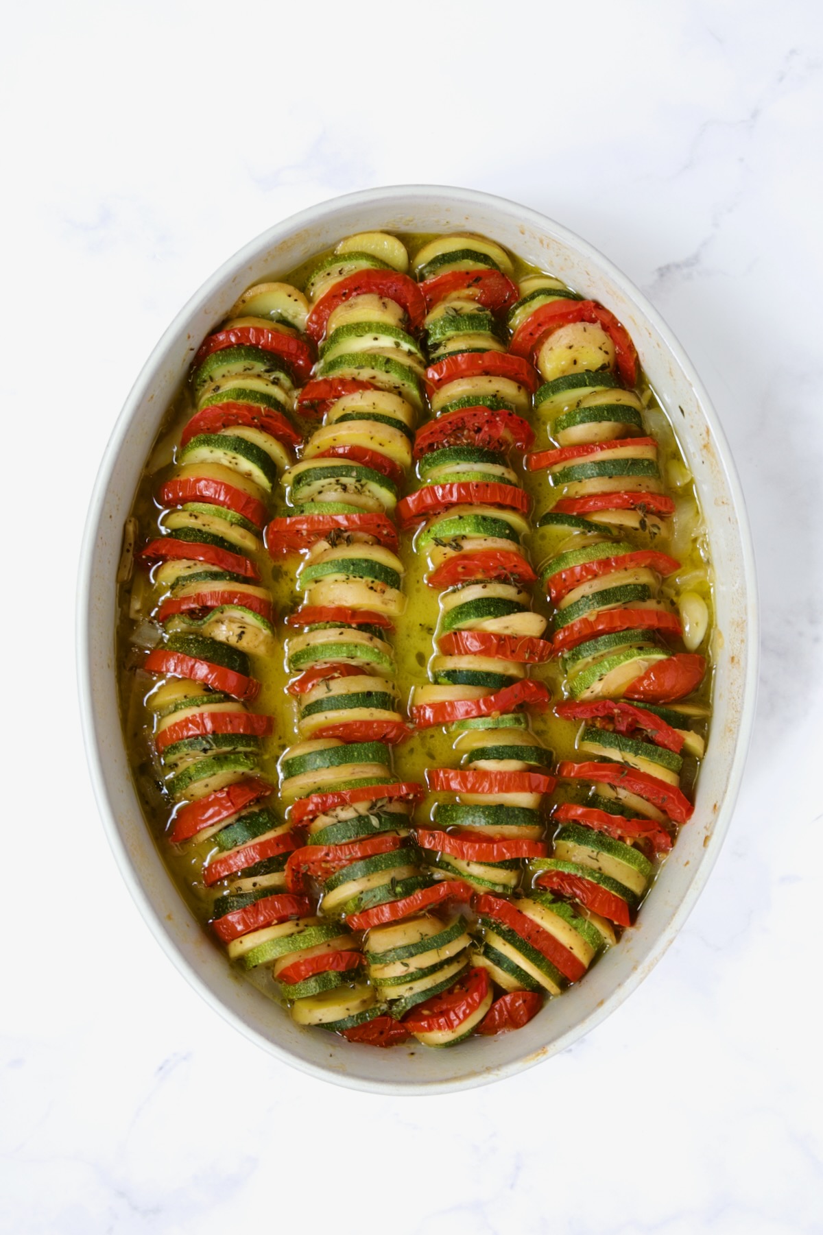 Baked zucchini, potatoes and tomatoes in oval baking dish.