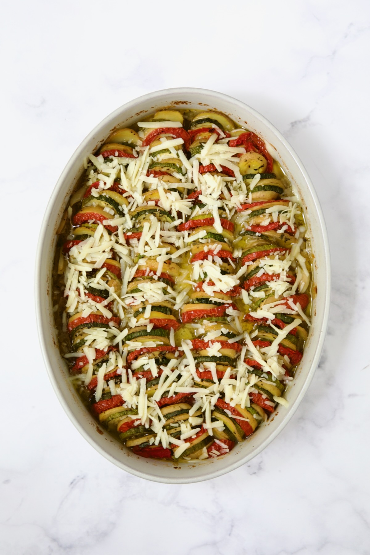 Cheese added to cooked vegetables in oval baking dish.