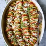 Vegetable Tian in oval baking dish with serving spoon garnished with fresh thyme.