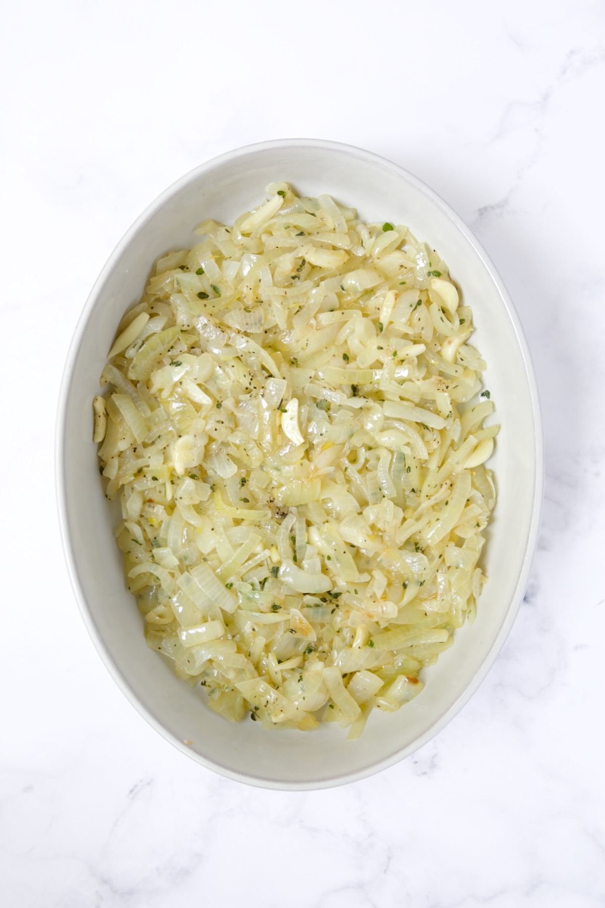 Onion, garlic and thyme mixture in oval baking dish.