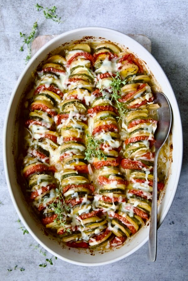 Vegetable Tian in oval baking dish with serving spoon garnished with fresh thyme.