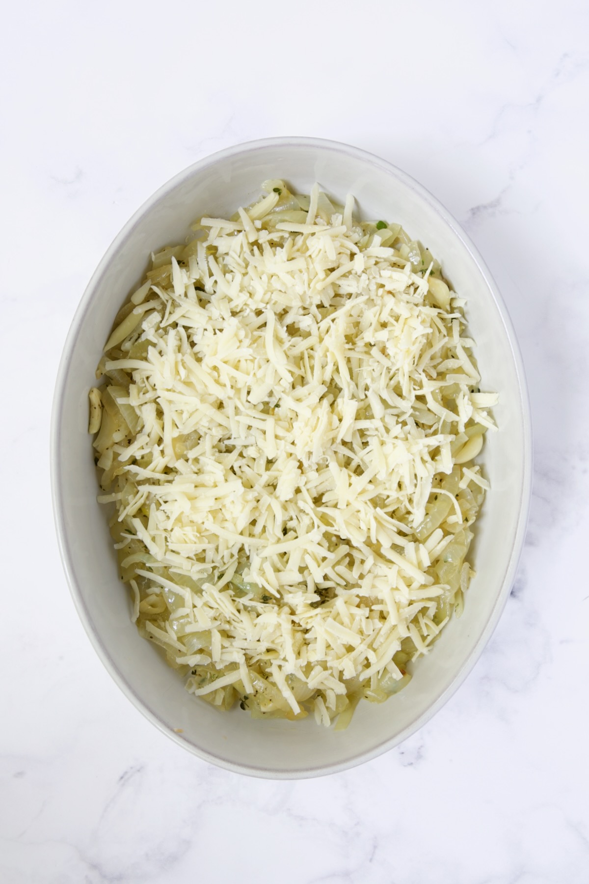 Cheese added to onion, garlic and thyme combination in oval baking dish.