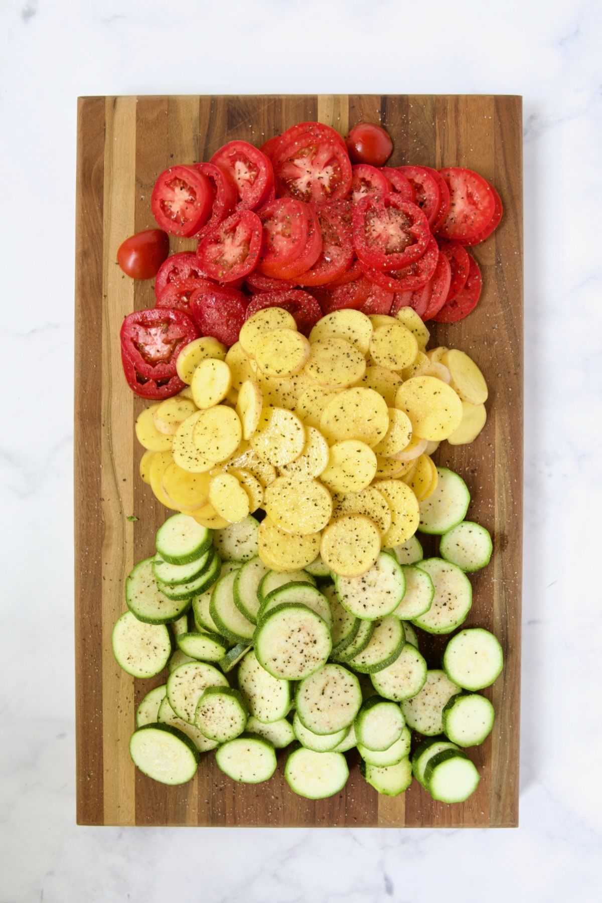 Sliced tomatoes, sliced Yukon Gold potatoes and sliced zucchini on wood cutting board.