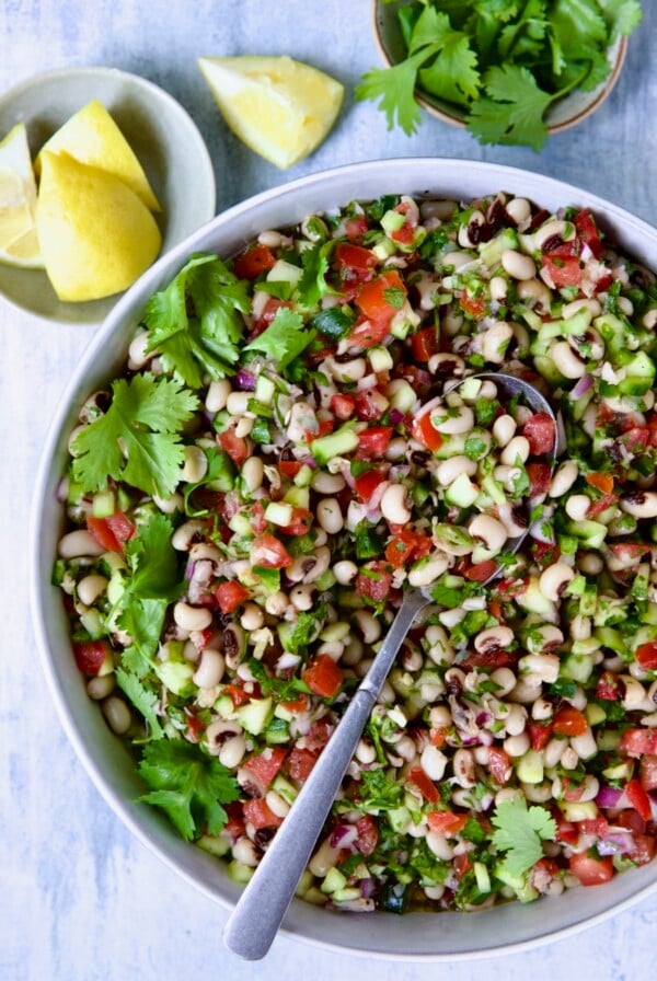 Black-Eyed Pea Salad in white bowl with lemon wedges and cilantro in bowls.
