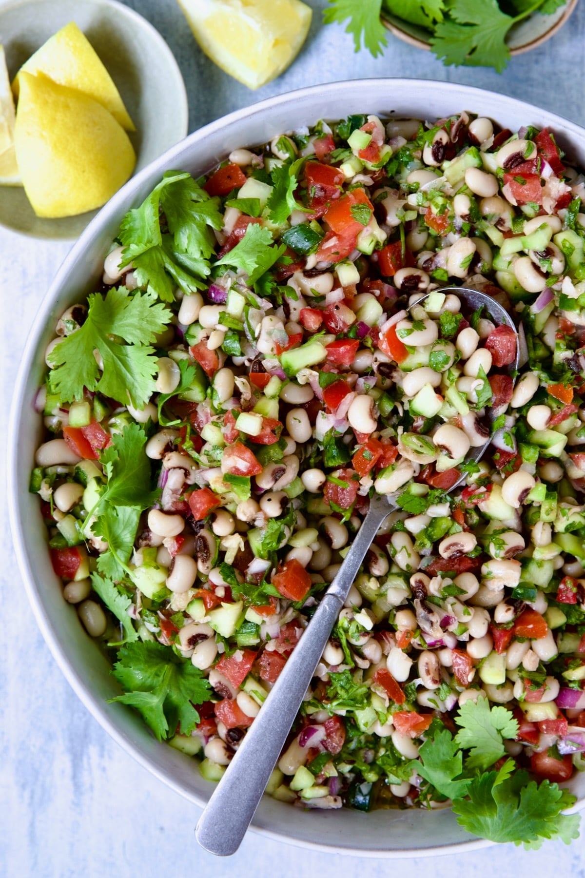 Black-Eyed Pea Salad in white bowl with lemon wedges and cilantro in bowls.