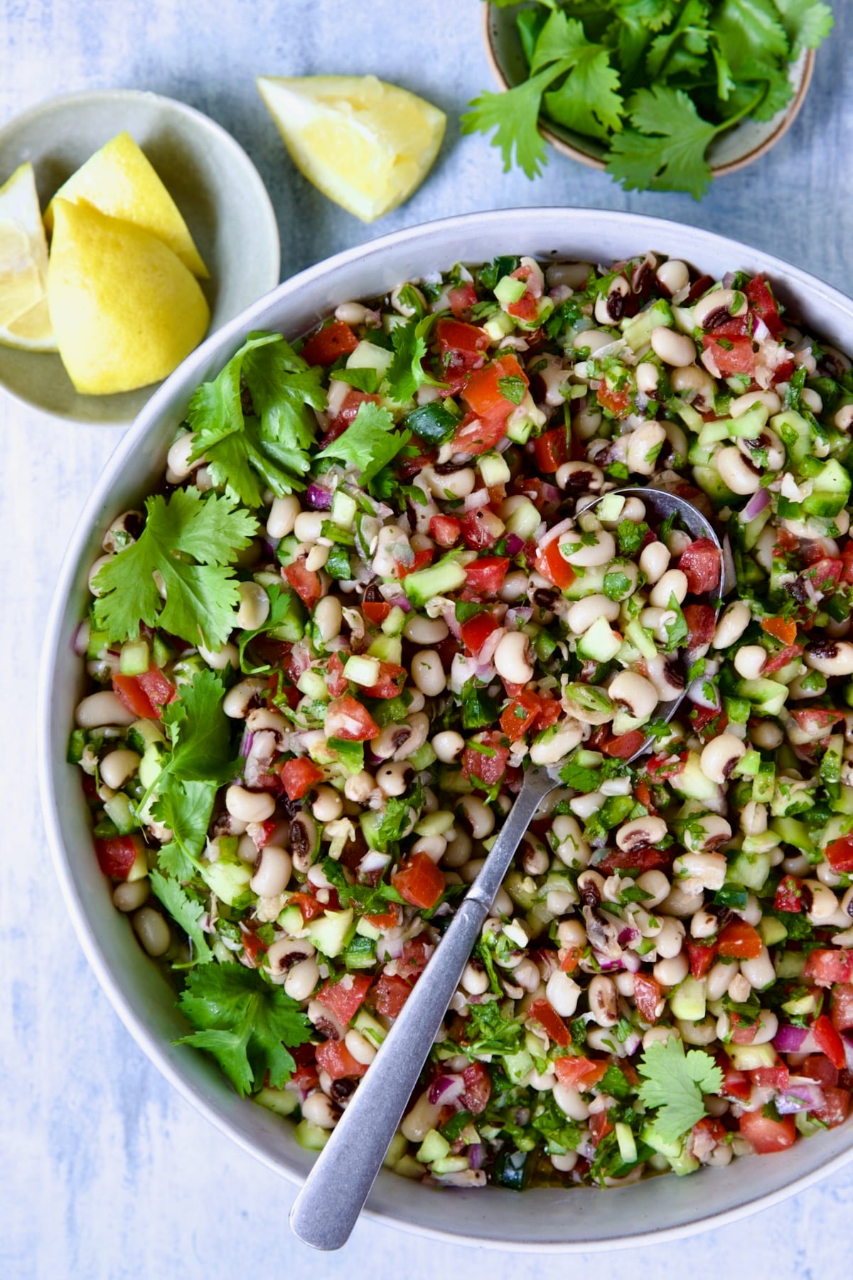 Black-Eyed Pea Salad in white bowl with lemon wedges and cilantro in bowls.