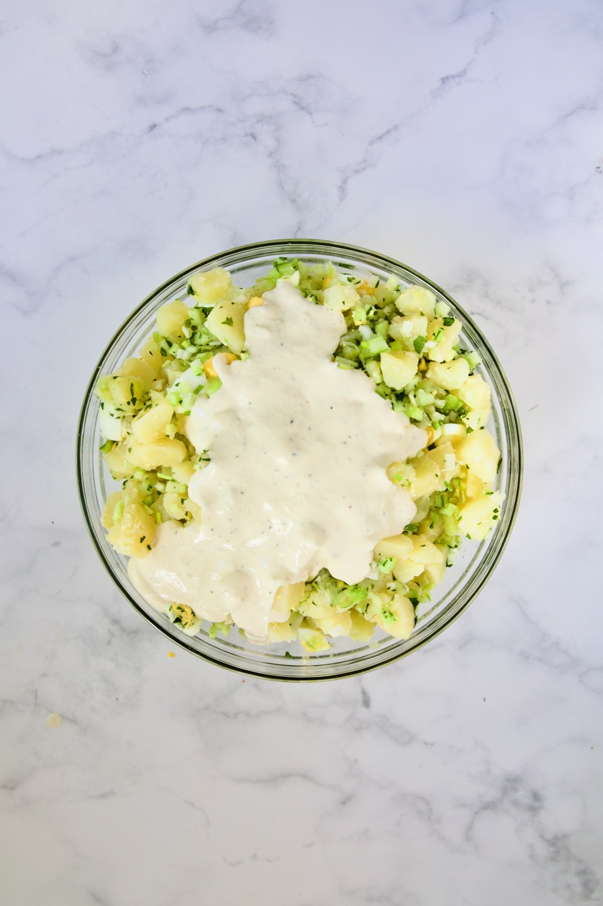 Dressing added to potato salad in glass bowl.
