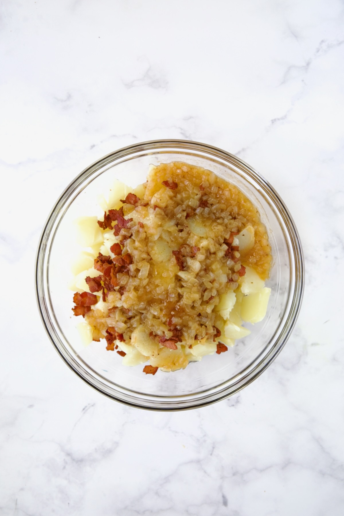 Potatoes and bacon with dressing poured over in glass bowl.
