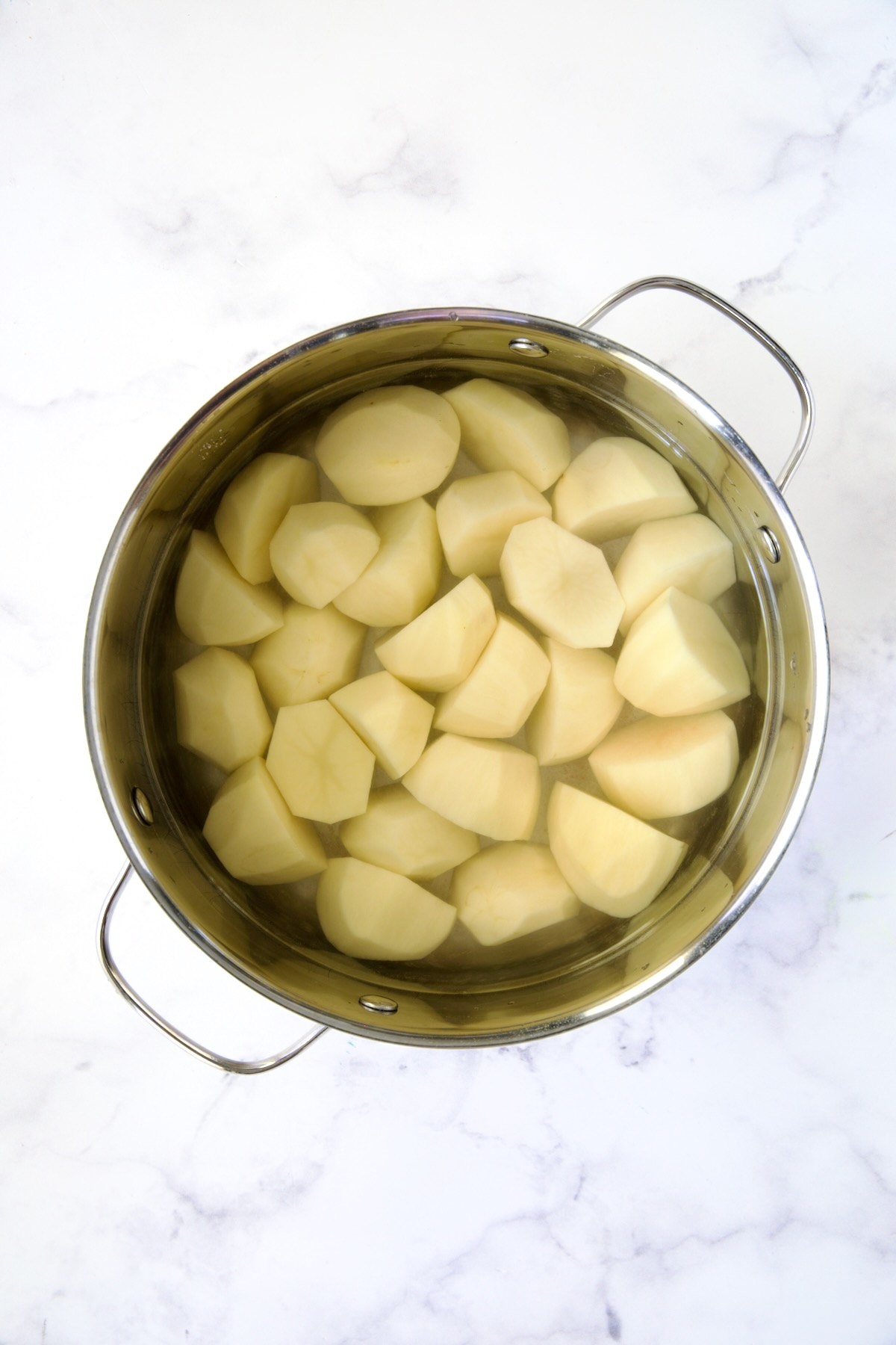 Uncooked potatoes in water in stainless steel pot.