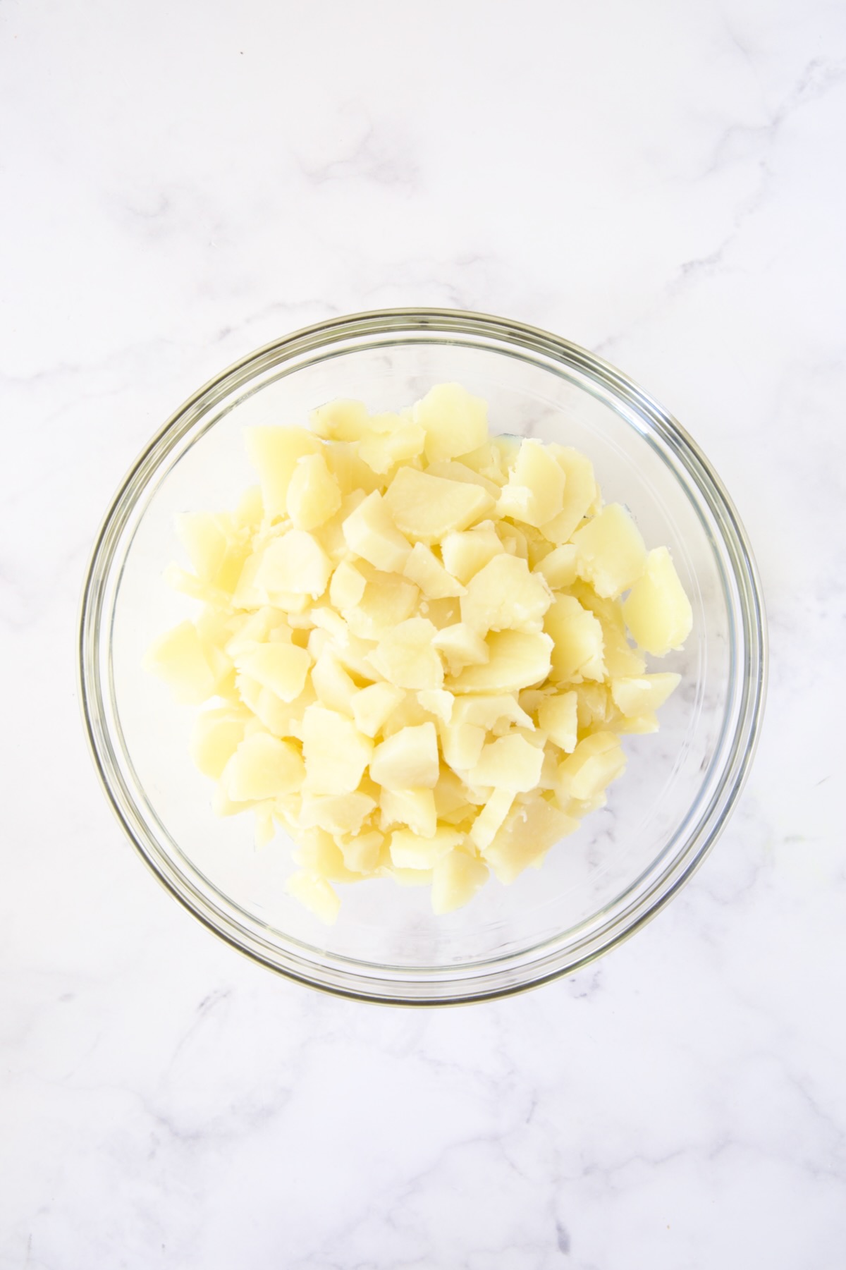 Cooked sliced potatoes in glass bowl.