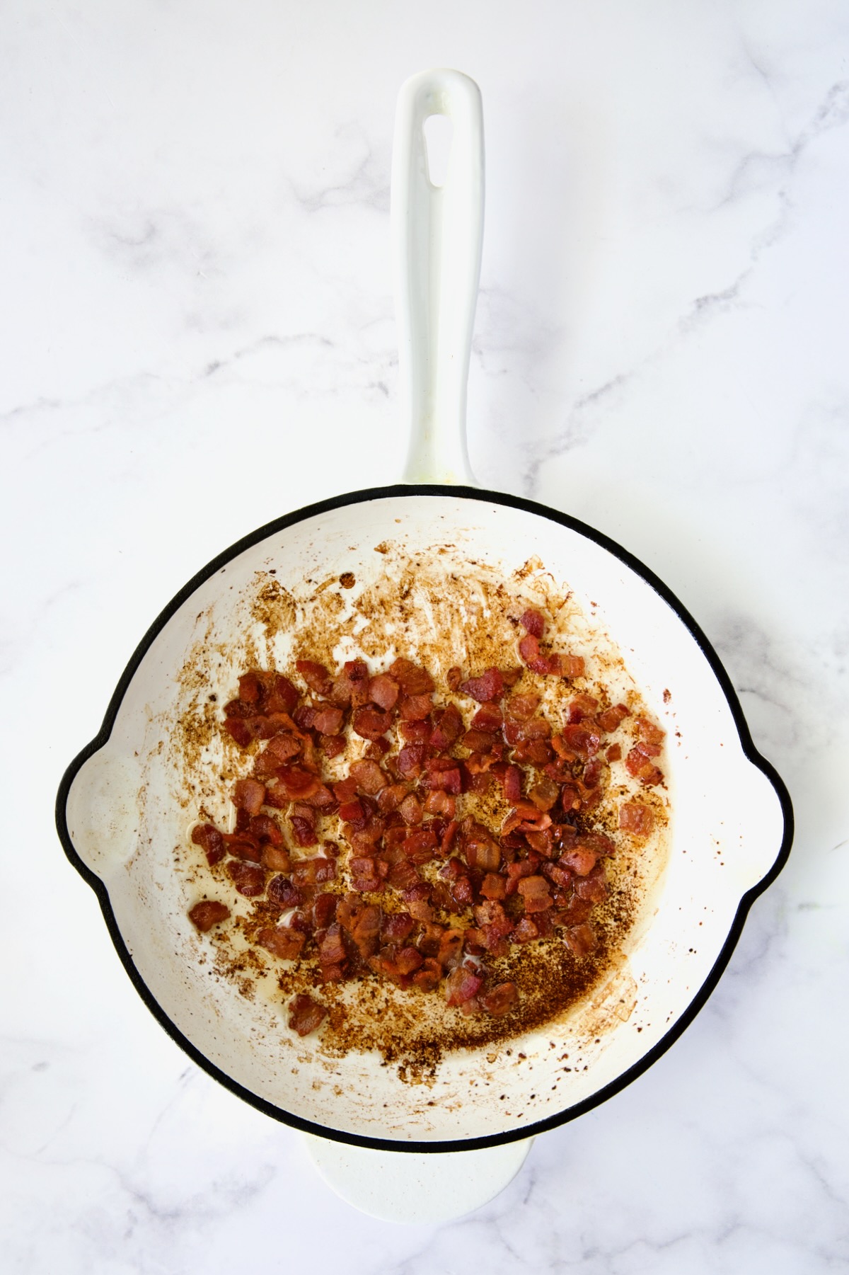 Cooked bacon in white enamel cast iron skillet.