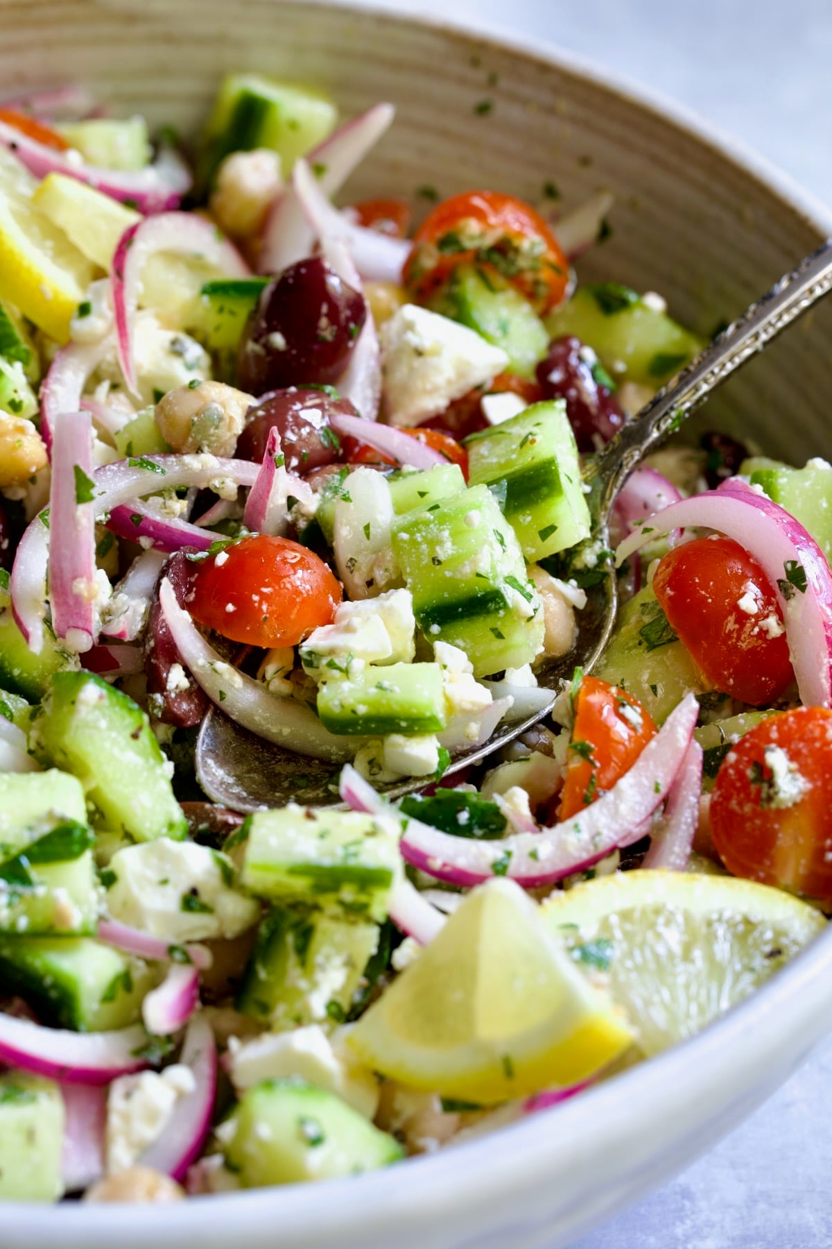 Greek Cucumber Salad in white bowl garnished with fresh lemon wedges.