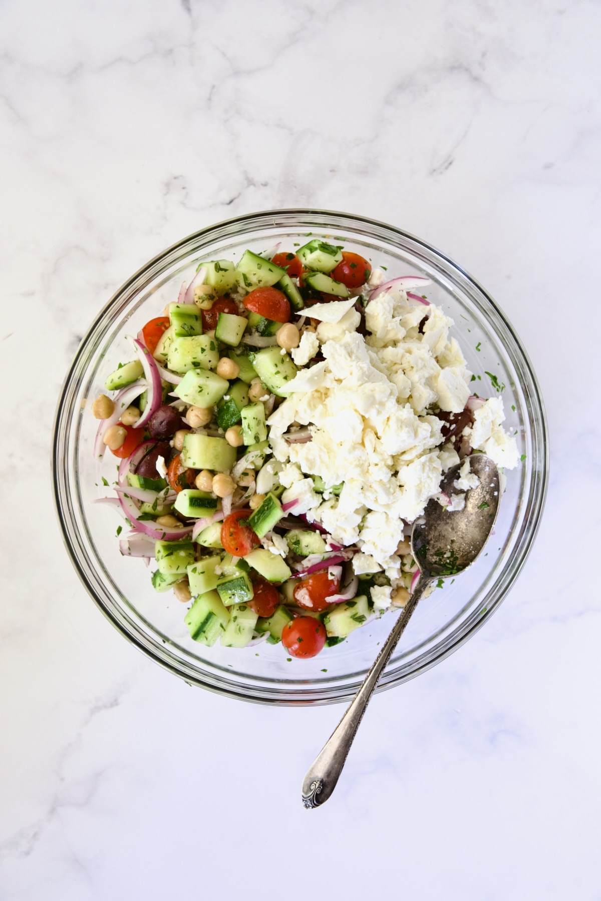 Ingredients for Greek Cucumber Salad in glass bowl after being mixed together with feta cheese added.
