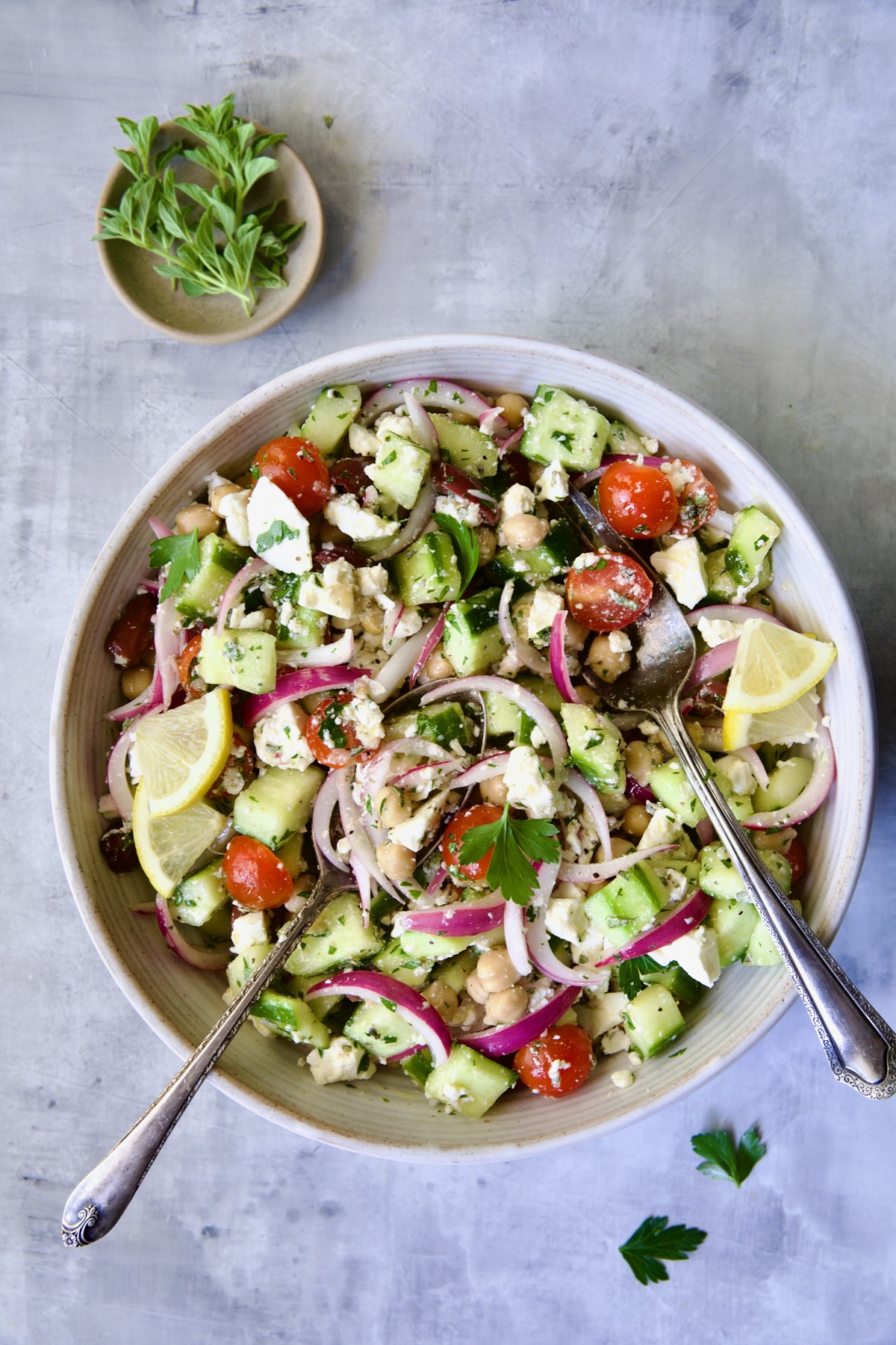 Greek Cucumber Salad in white serving bowl with serving utensils.
