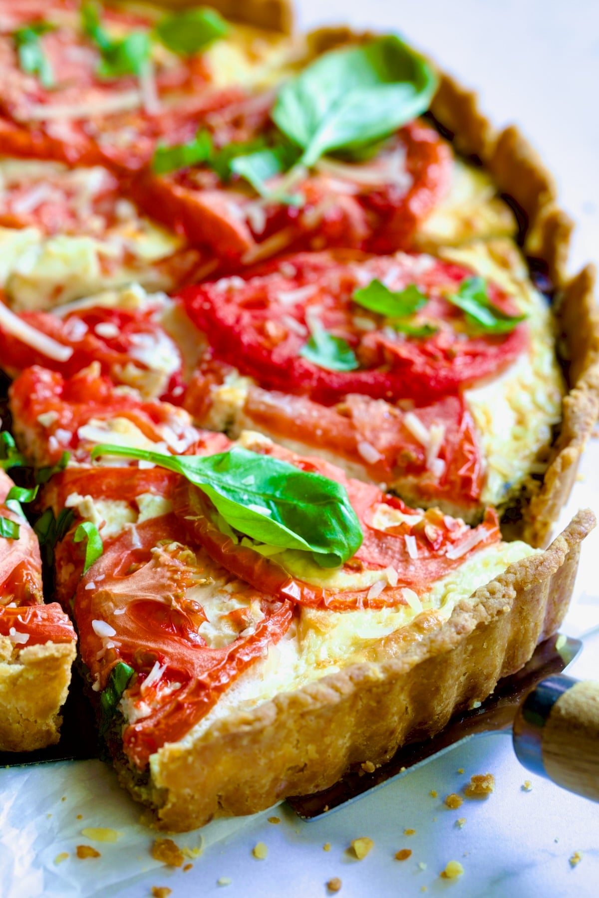 Tomato Tart with Ricotta and Cheese garnished with fresh basil leaves cut into wedges with pie server picking up a piece.