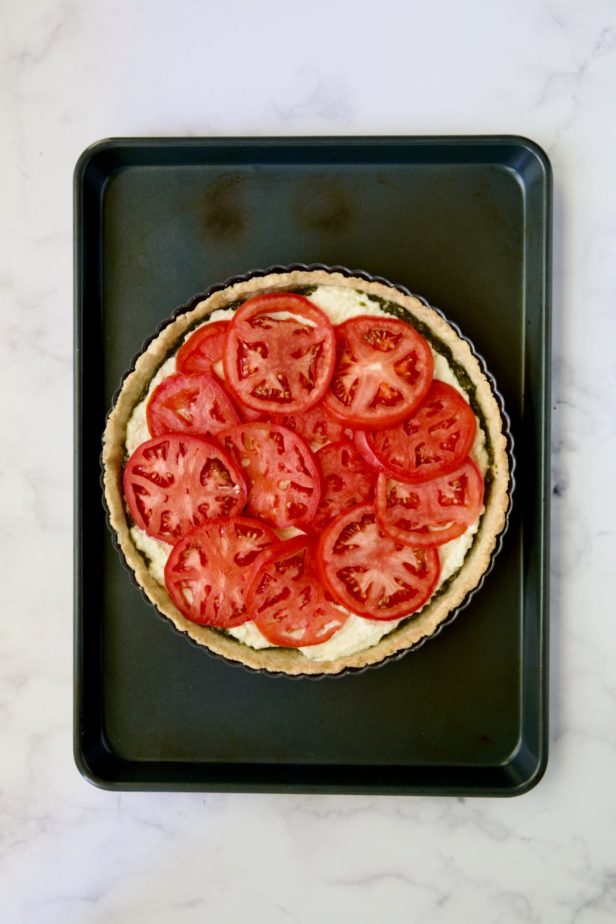 Tomatoes placed over ricotta and pesto in tart pan.