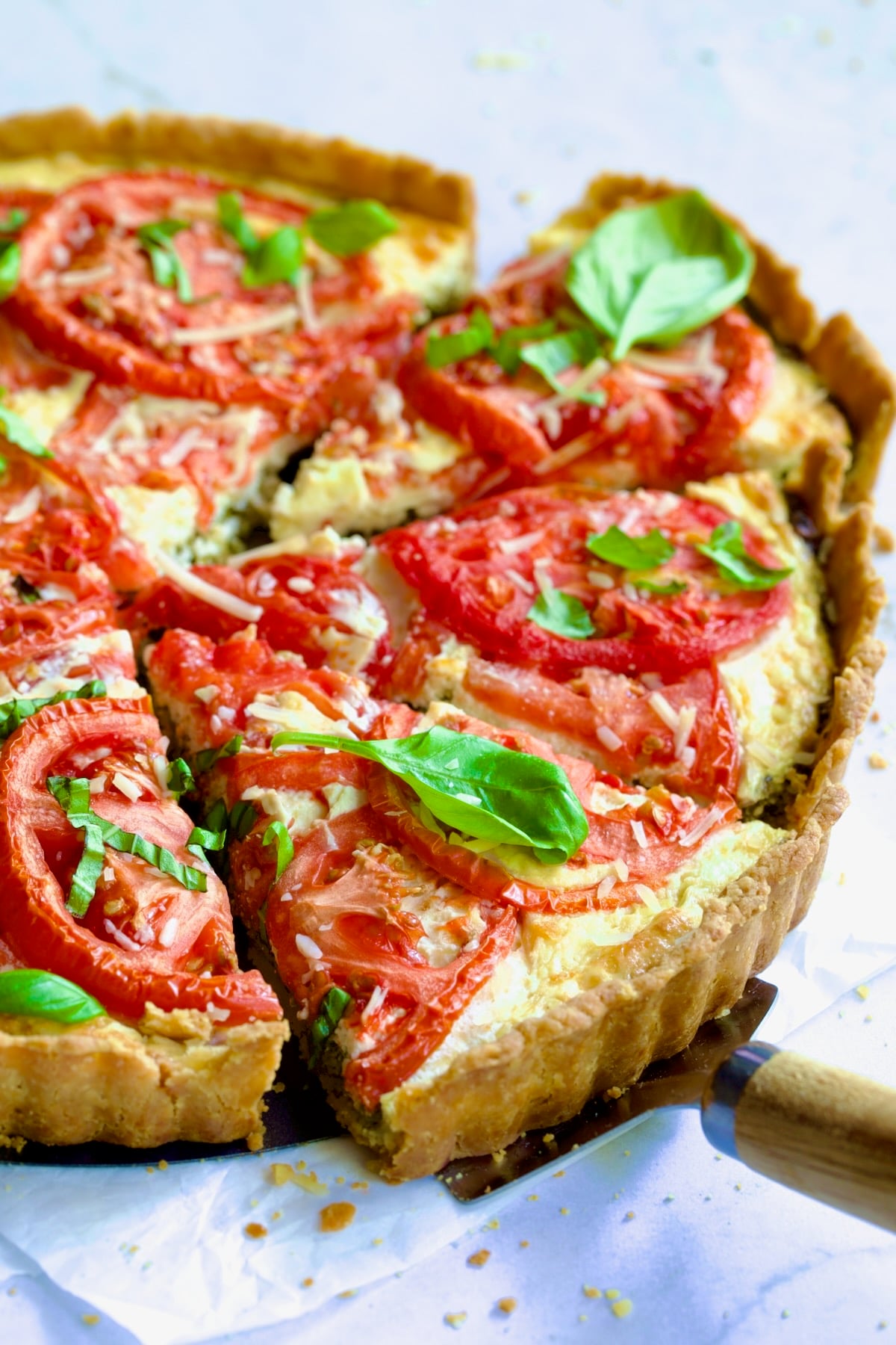 Tomato Tart with Ricotta and Cheese garnished with fresh basil leaves cut into wedges with pie server picking up a piece.