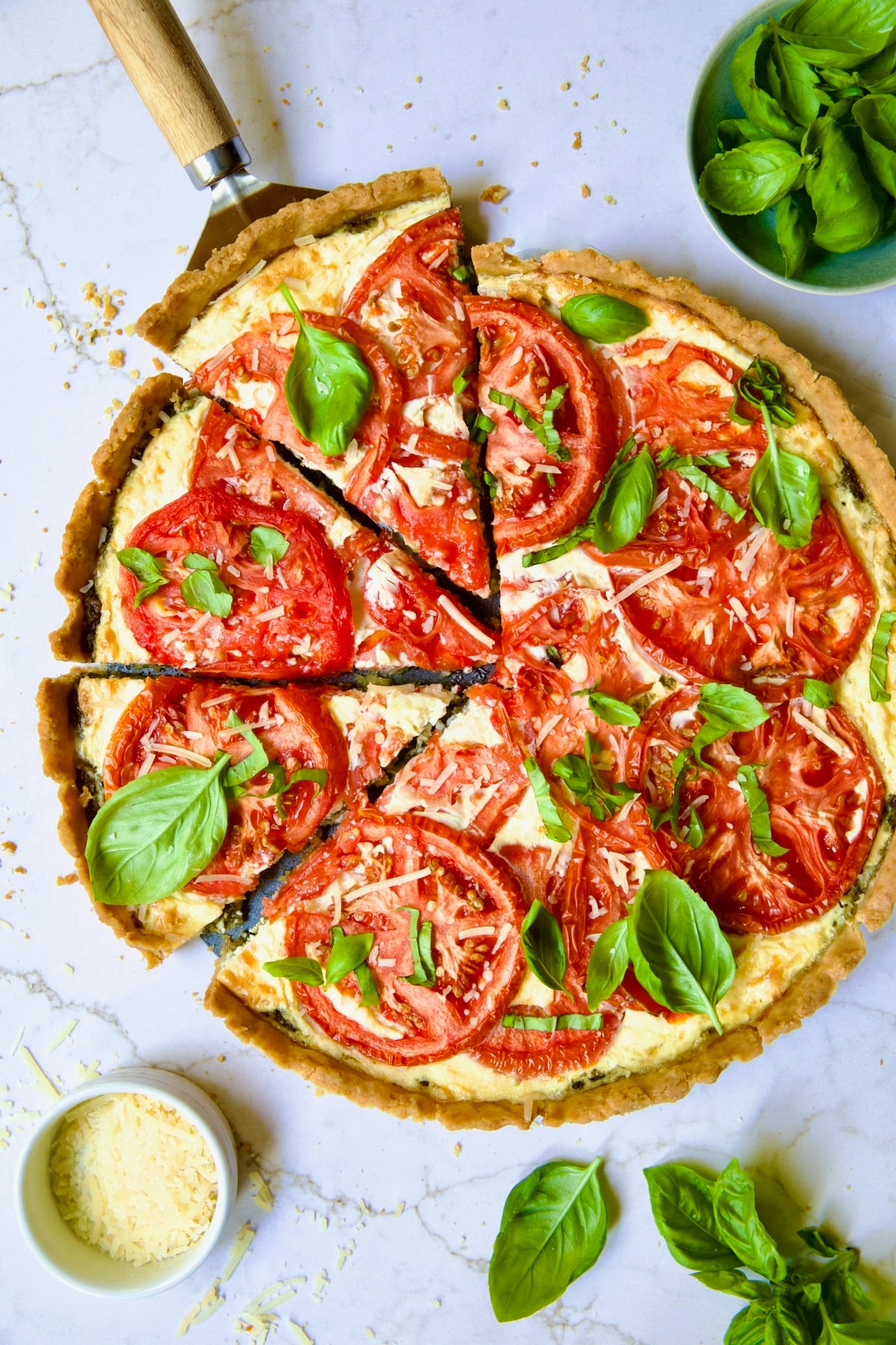 Tomato Tart with Ricotta and Cheese garnished with fresh basil leaves cut into wedges with pie server picking up a piece.