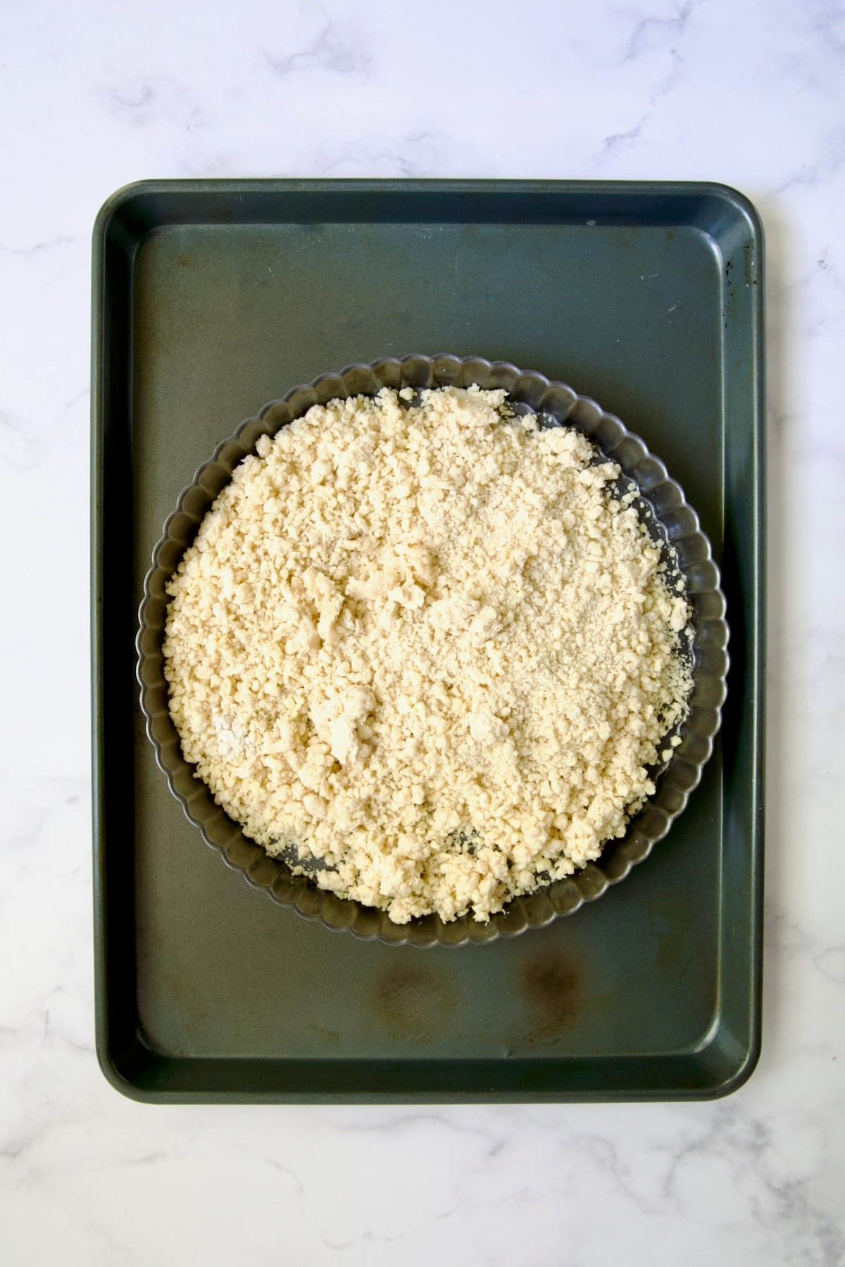 Tart crust dough in pan on rimmed sheet pan before being spread into tart pan.