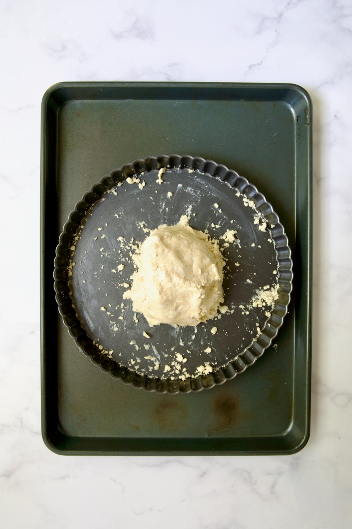 Tart dough gathered into a ball in tart pan on rimmed sheet pan.