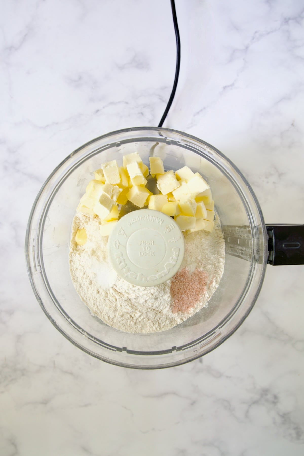 Butter cubes, flour, salt and pepper in bowl of food processor.