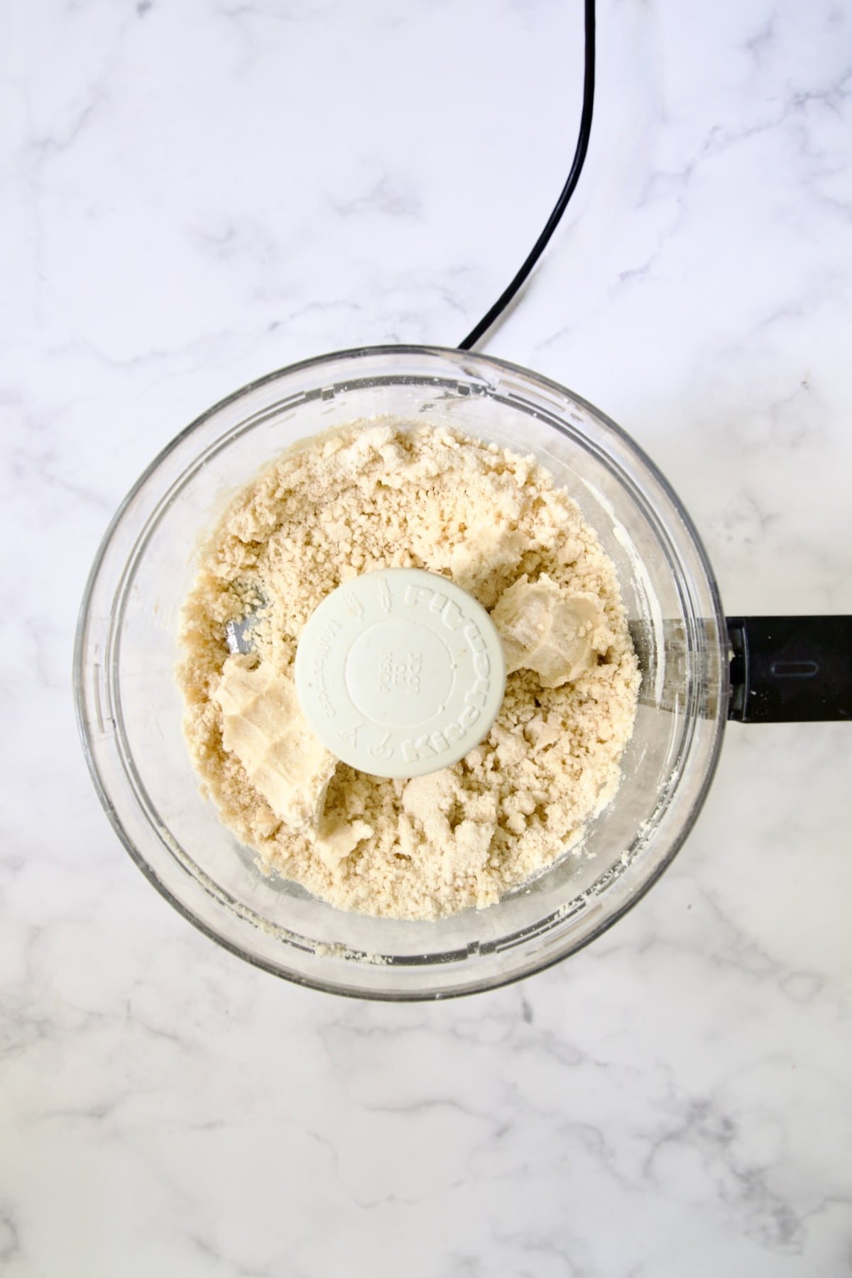 Butter cubes, flour, salt and pepper in bowl of food processor with ice water added demonstrating how it holds together.