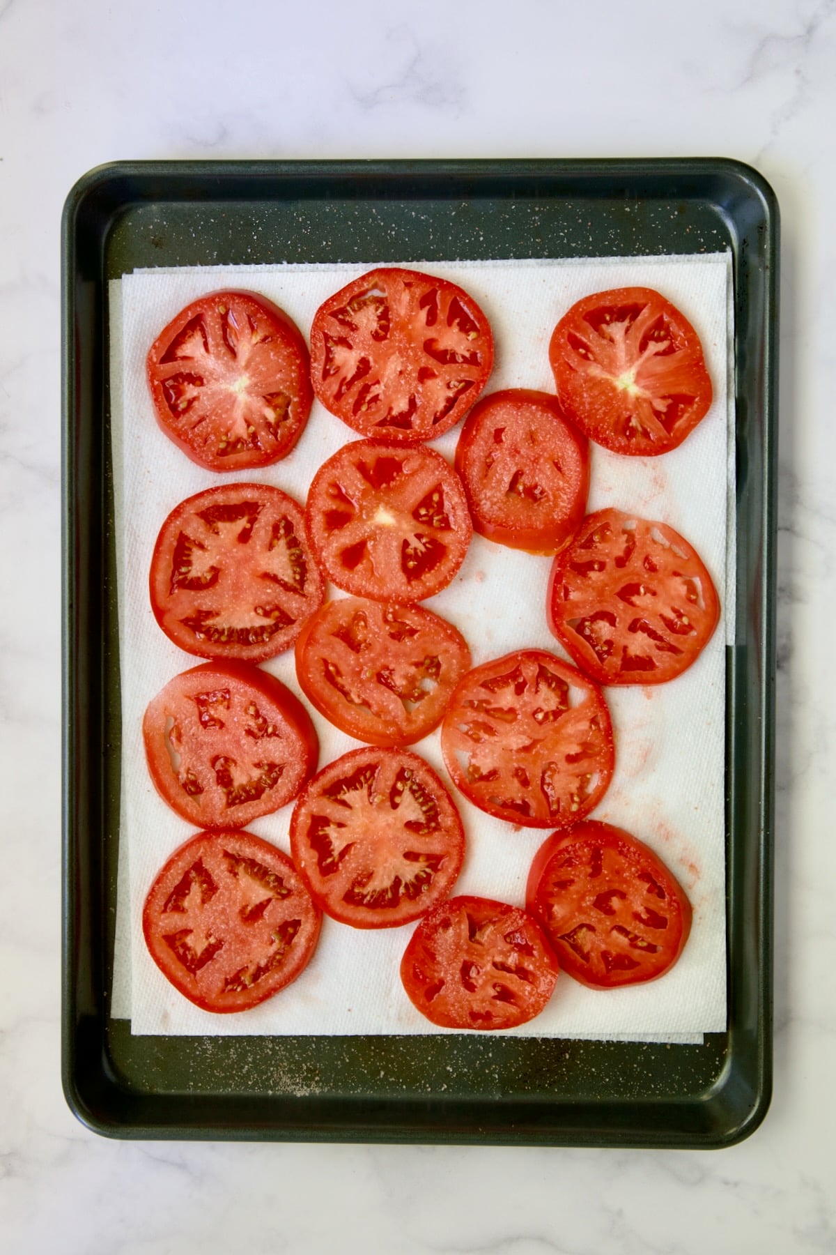 Sliced tomatoes draining on paper towel-lined rimmed baking sheet.