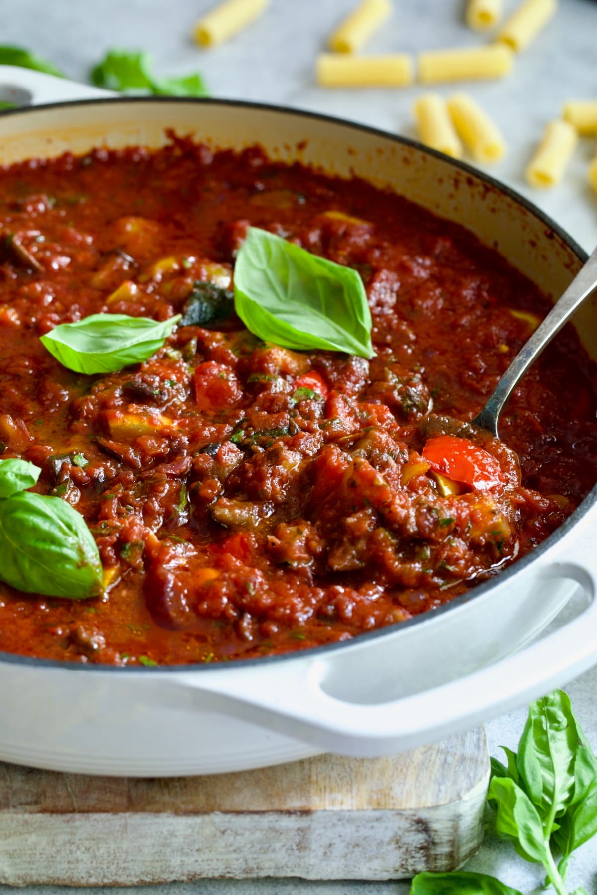 Veggie Pasta Sauce in white enamel cast iron skillet with serving spoon garnished with fresh basil.