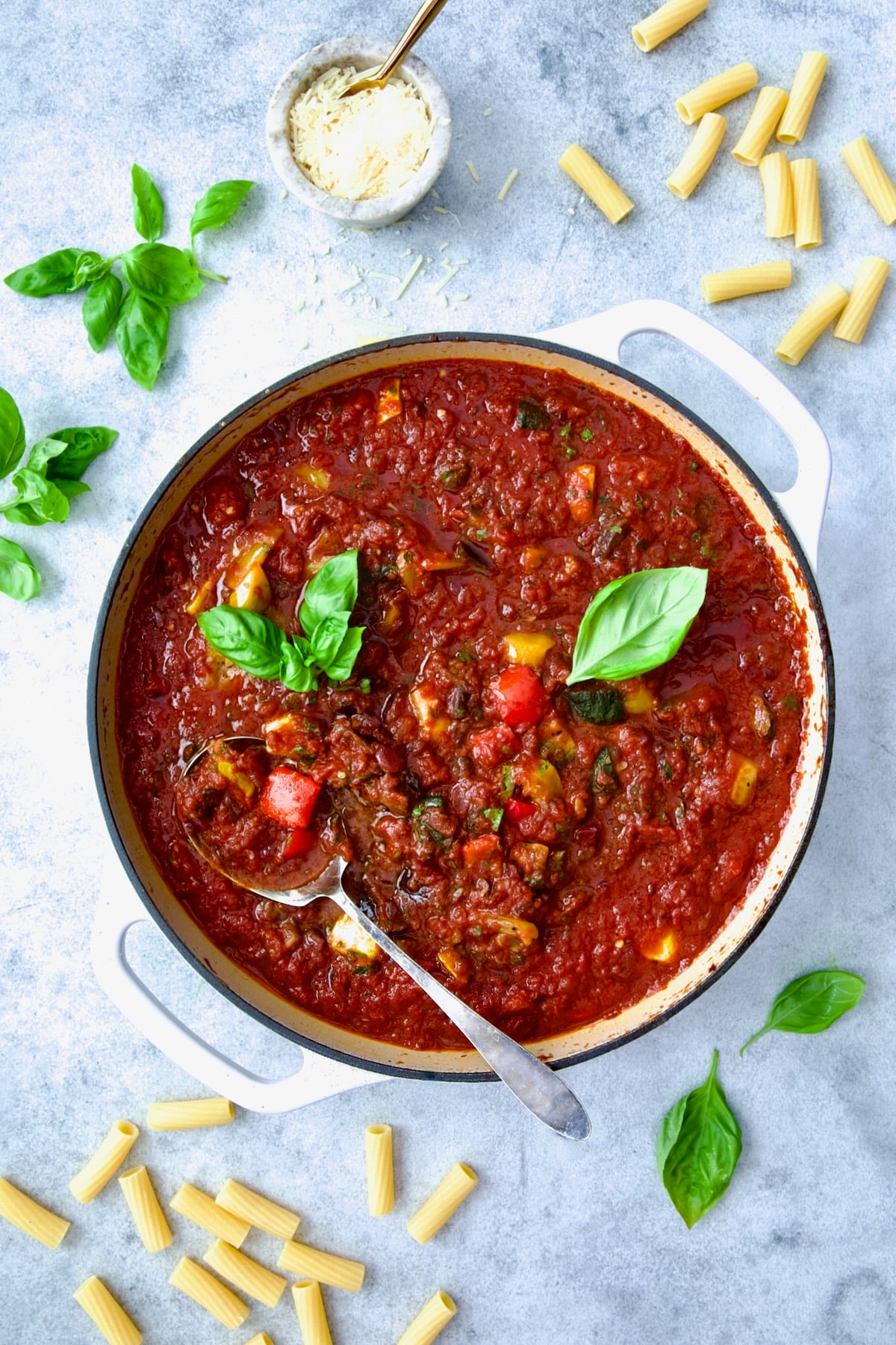 Veggie Pasta Sauce in white enamel cast iron skillet with serving spoon garnished with fresh basil.