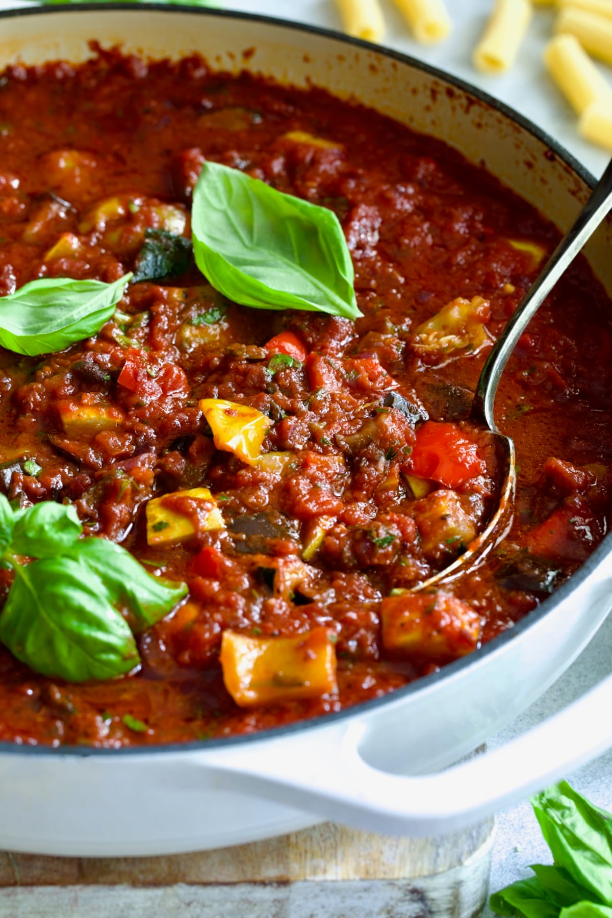 Veggie Pasta Sauce in white enamel cast iron skillet with serving spoon garnished with fresh basil.