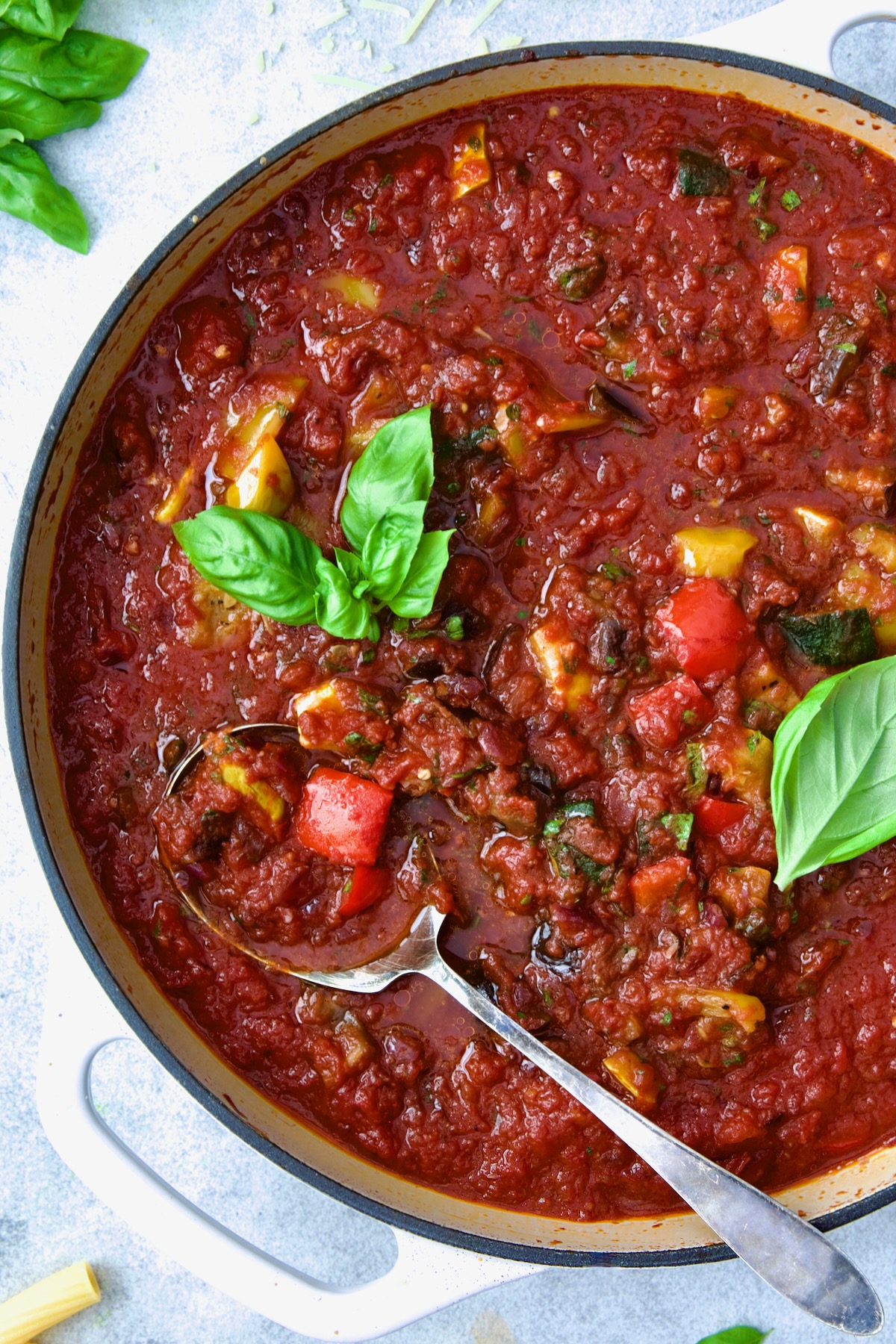 Veggie Pasta Sauce in white enamel cast iron skillet with serving spoon garnished with fresh basil.