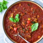 Veggie Pasta Sauce in white enamel cast iron skillet with serving spoon garnished with fresh basil.