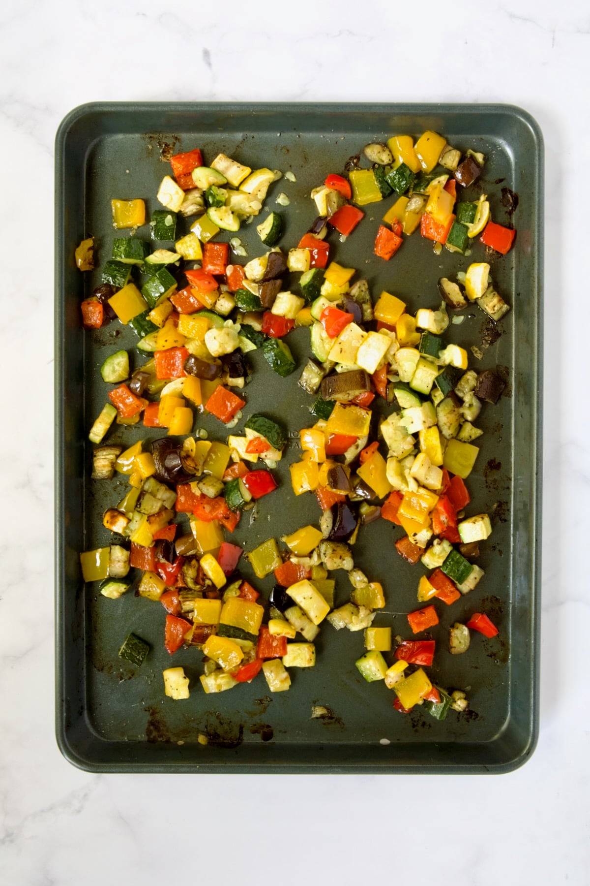 Cubed zucchini, yellow squash, eggplant, yellow and red bell pepper on rimmed sheet pan after being roasted.