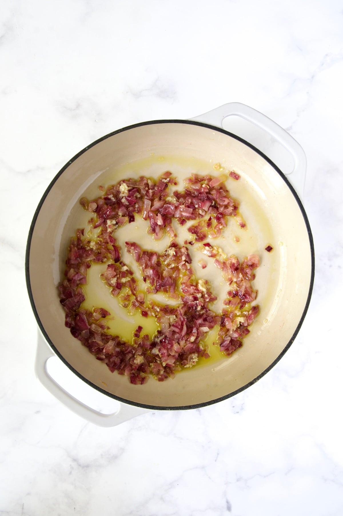 Cooked red onion in white enamel cast iron skillet.