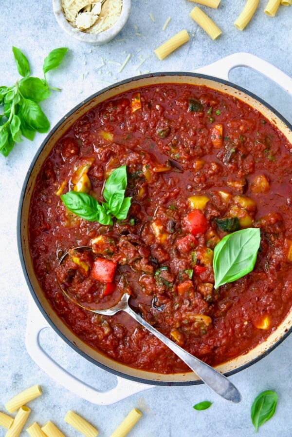 Veggie Pasta Sauce in white enamel cast iron skillet with serving spoon garnished with fresh basil.