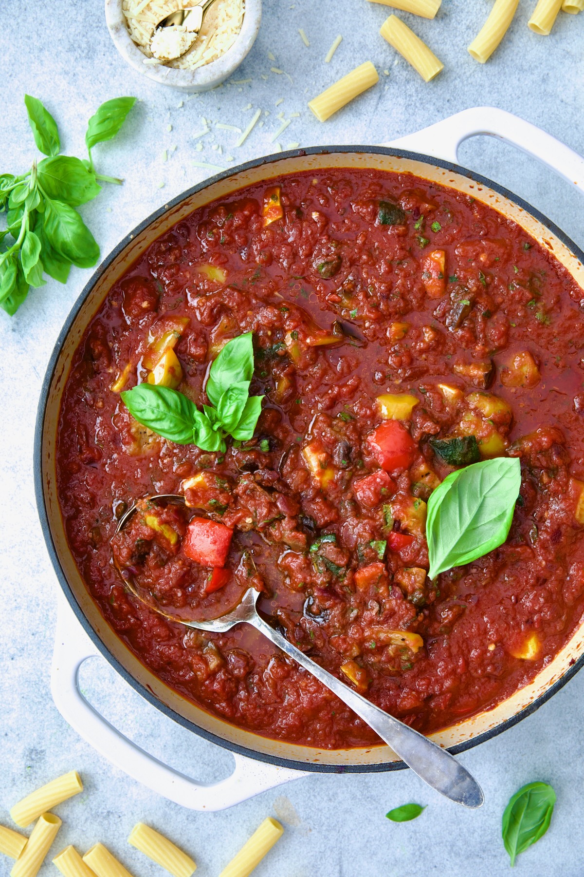 Veggie Pasta Sauce in white enamel cast iron skillet with serving spoon garnished with fresh basil.