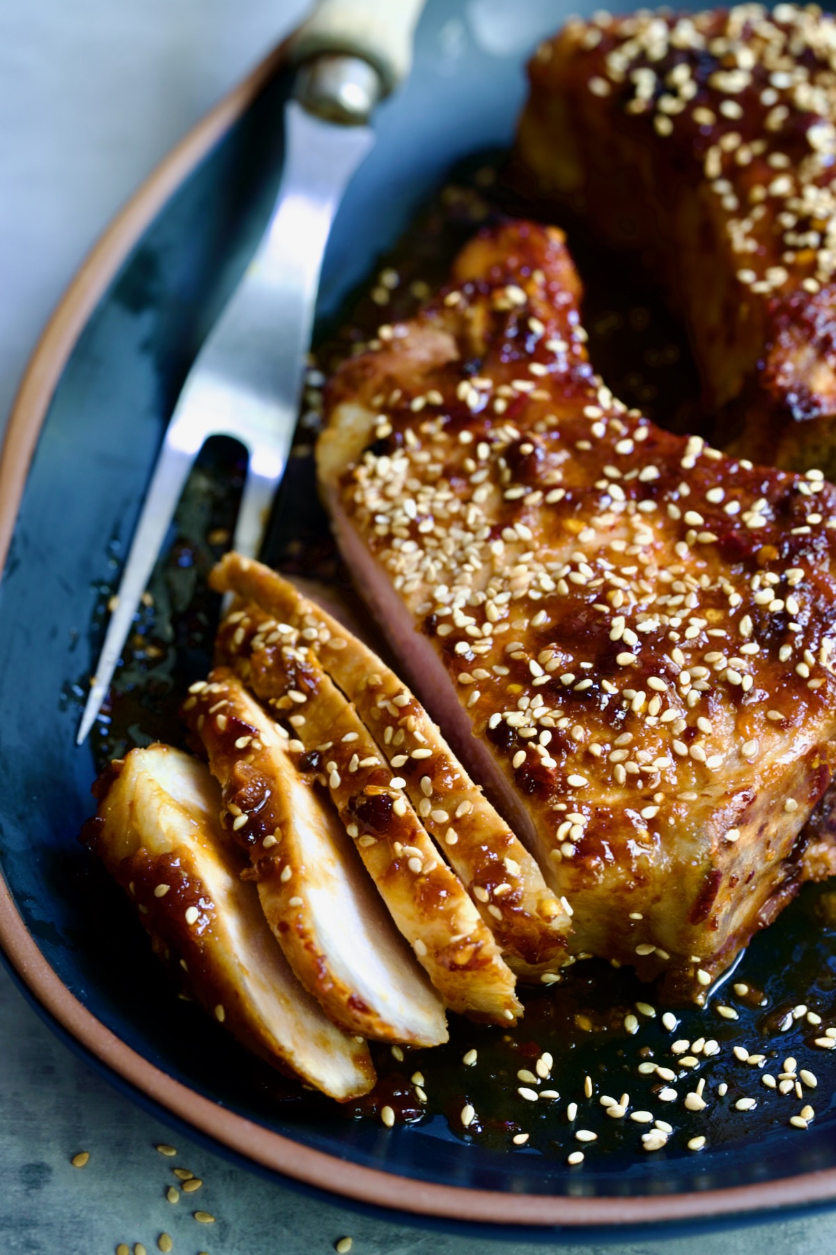 Partially sliced Asian Pork Chop on a black platter garnished with sesame seeds.