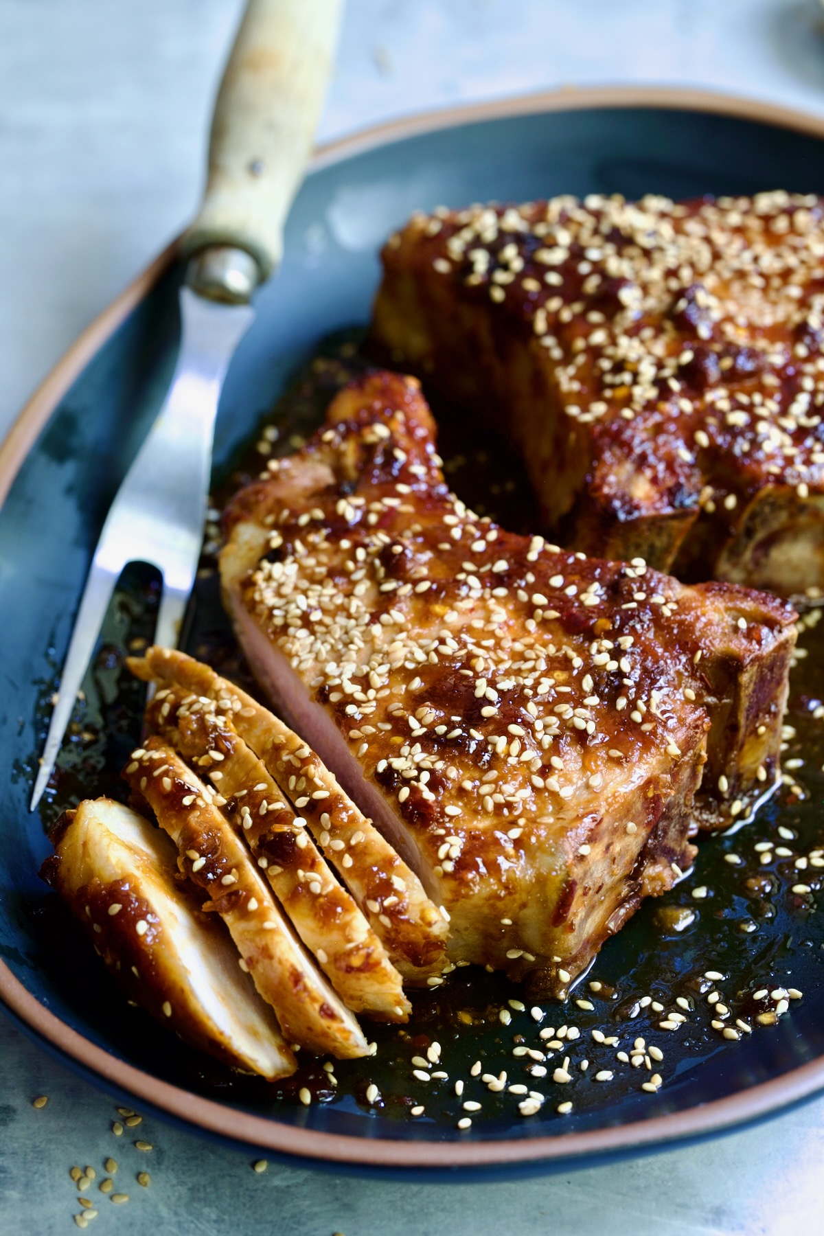 Two Asian Pork Chops on black oval platter garnished with sesame seeds with one pork chop partially sliced.