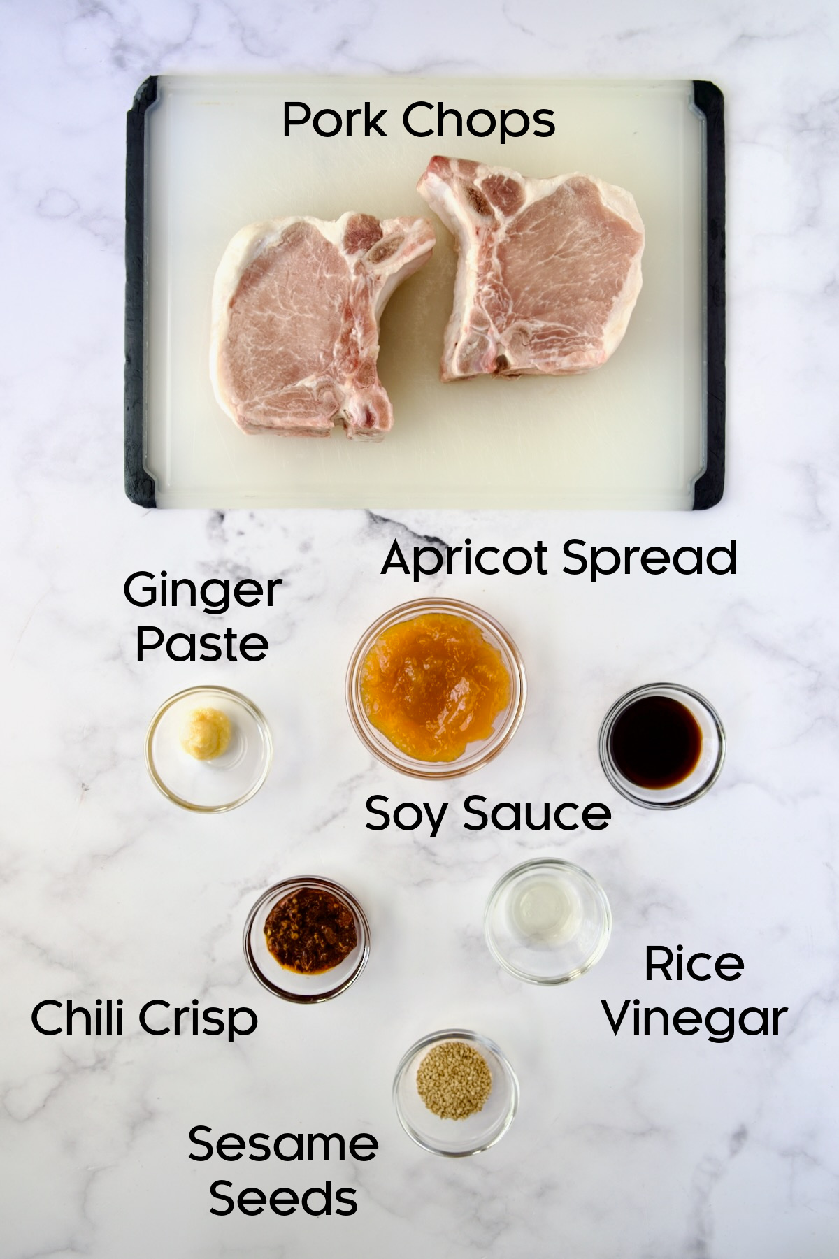 Ingredients for Asian Pork Chops in glass bowls with two uncooked pork chops on white cutting board.