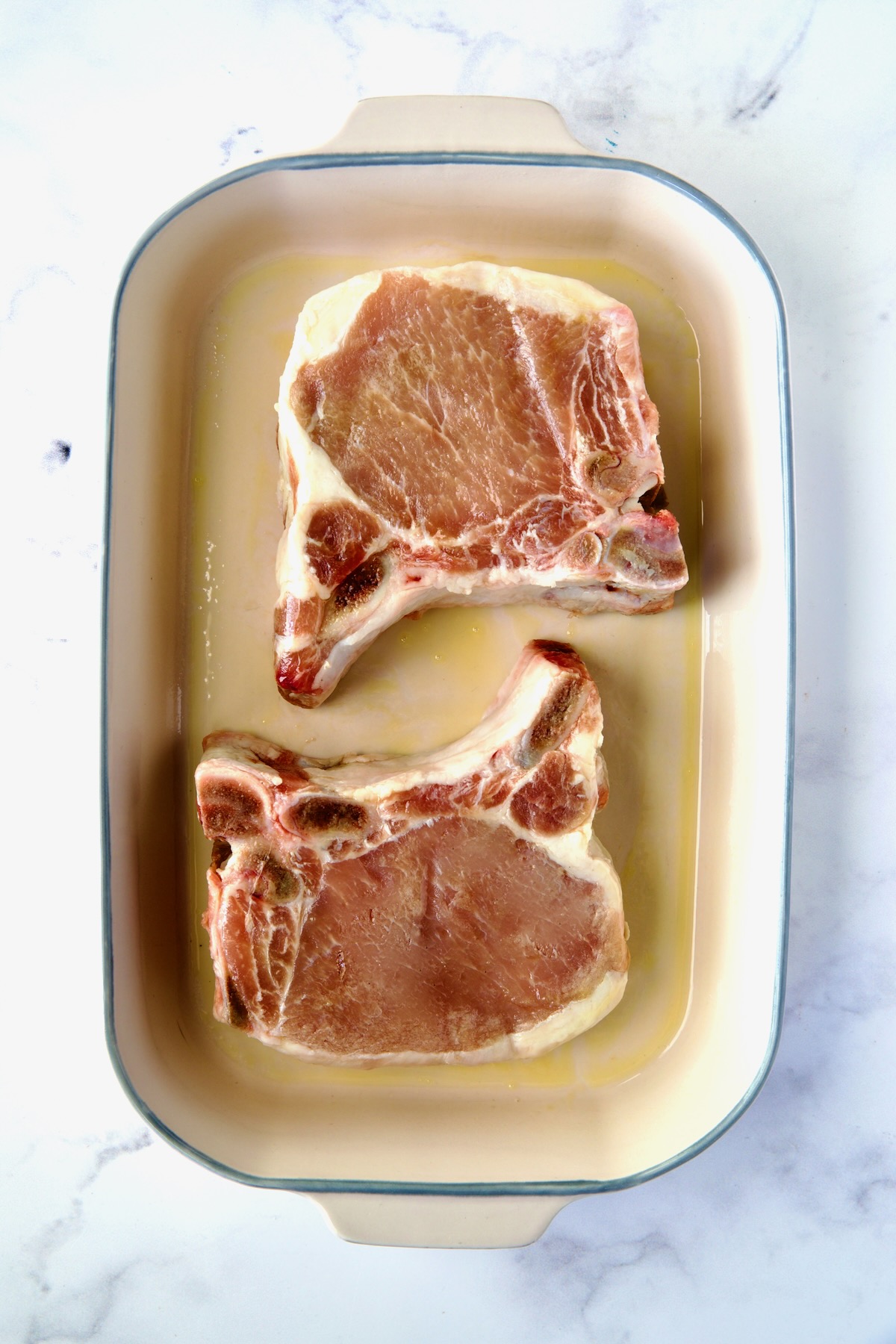 Two uncooked pork chops in baking dish.