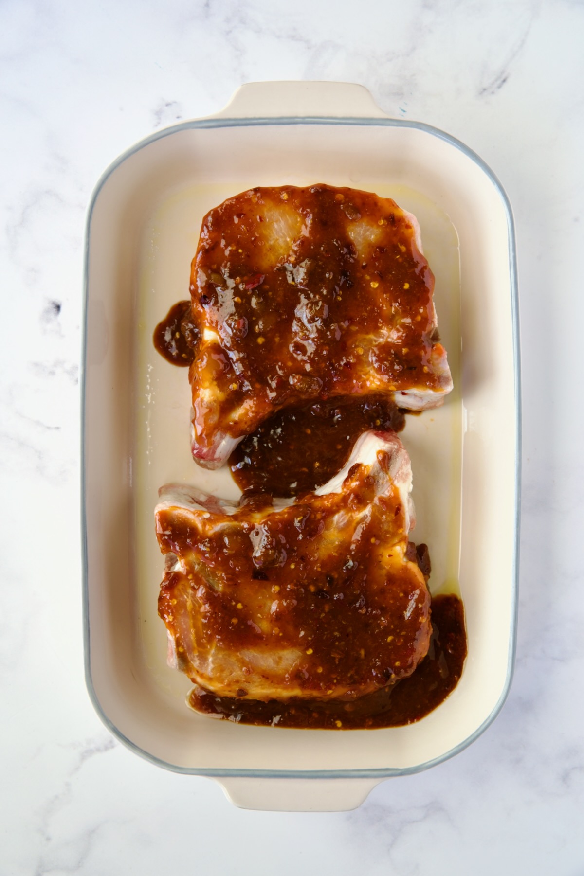 Two pork chops in baking dish with glaze poured over them.