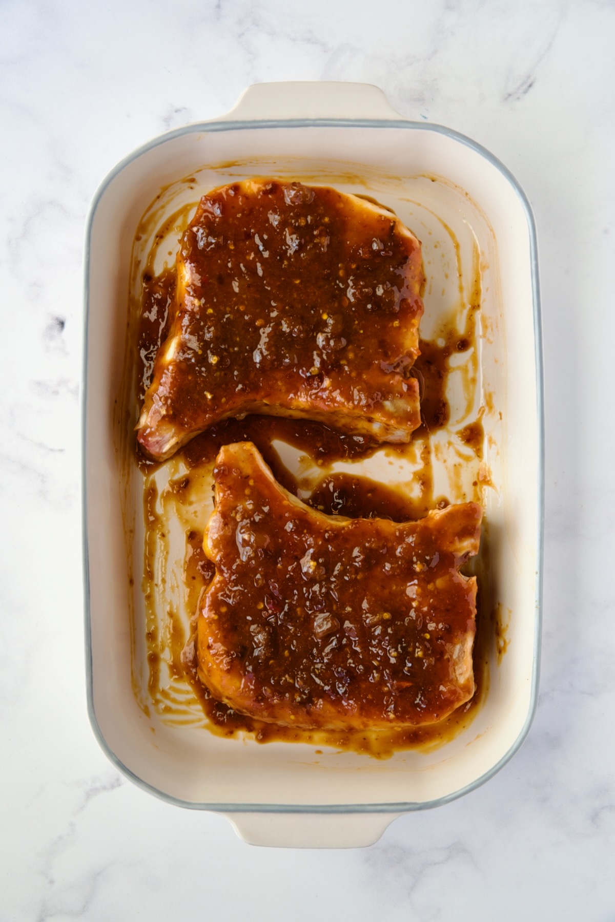 Two pork chops in baking dish with glaze poured over both sides.